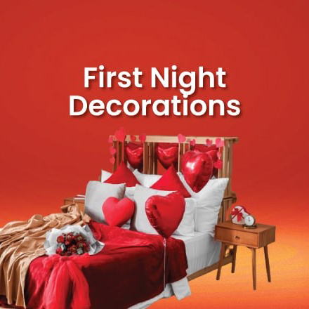 A romantic first night room decoration featuring a beautifully made bed with red and white linens, heart-shaped foil balloons, a bouquet of red roses, and a heart garland on the headboard.