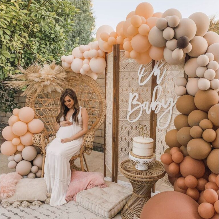 An elegant baby shower decoration setup in Gurgaon, featuring a gold sequin backdrop, white and gold balloons, and floral arrangements