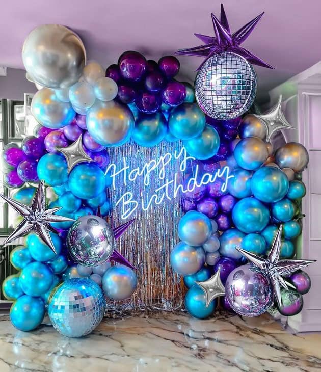 Transform your next celebration into a magical spectacle with our stunning Blue Purple Balloon Birthday Decor! Featuring a vibrant arch of chrome purple, blue, and silver balloons, a shimmering fringe backdrop, and a glowing neon "Happy Birthday" sign, this setup by Adore Celebration adds an unforgettable touch to any party in Gurgaon. Perfect for creating dazzling memories!