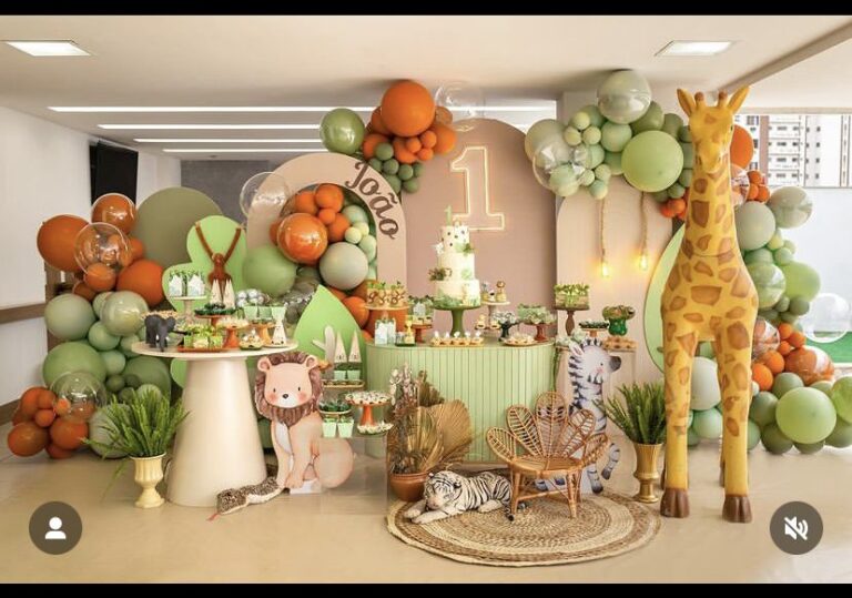 A vibrant jungle-themed birthday party setup with a large giraffe prop, various animal cutouts, and green, orange, and white balloons.