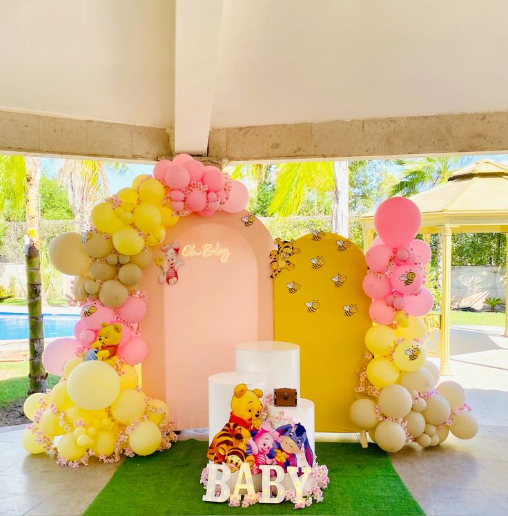 A vibrant Winnie the Pooh themed baby shower decoration featuring a pink arch backdrop with "Oh Baby" neon sign, a yellow arch with bee decals, balloon garlands in yellow, pink, and neutral tones, and Pooh character cutouts.